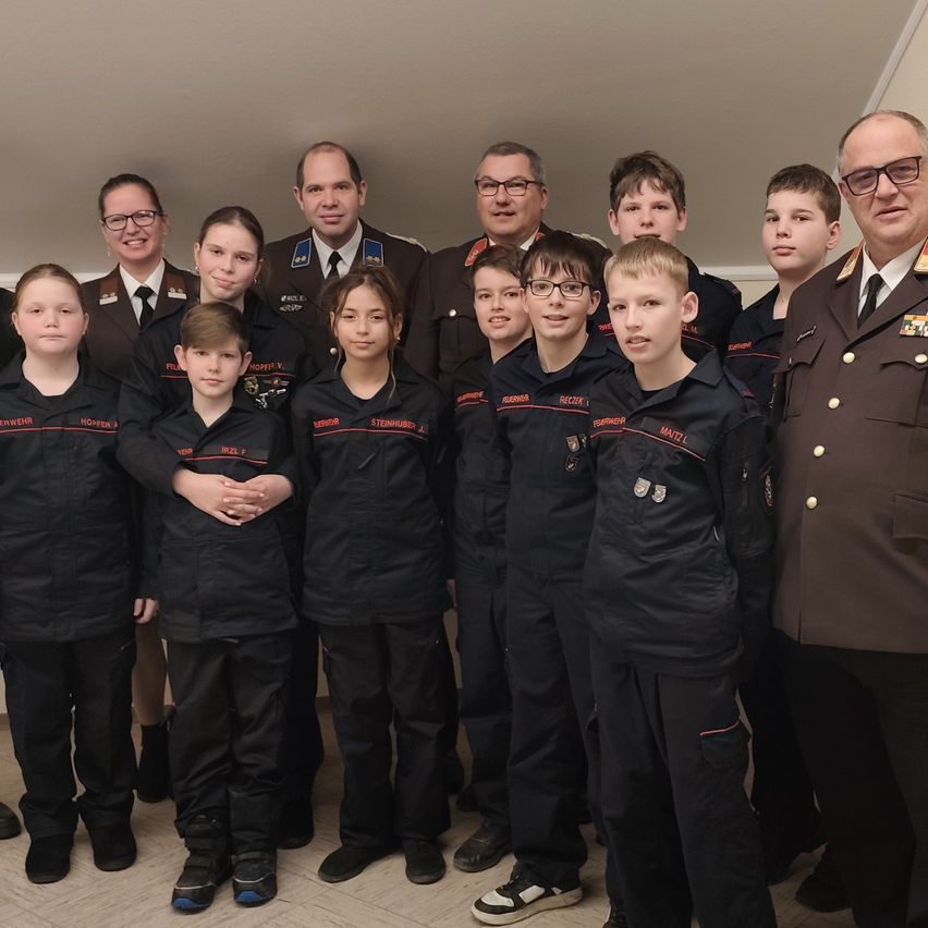 Eine Gruppe uniformierter Kinder und Erwachsener posiert für ein Foto, möglicherweise in einer Schule. Sie stehen in zwei Reihen, wobei Erwachsene in Militäruniformen im Hintergrund stehen.