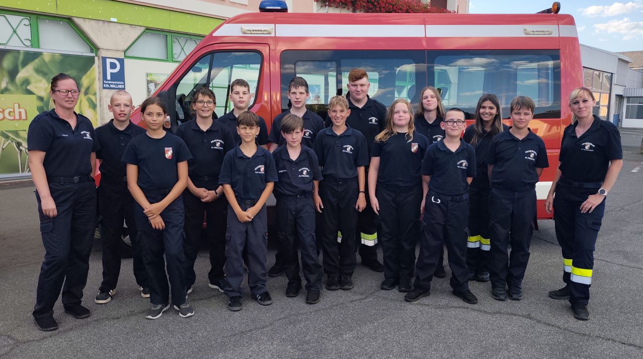 Eine Gruppe junger Menschen in Uniform, möglicherweise Feuerwehrleute, posiert für ein Foto vor einem roten Feuerwehrwagen.