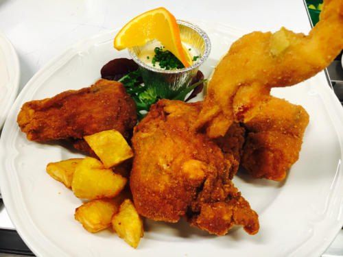 Ein Teller mit gebratenem Hühnchen, Kartoffeln und einer Dip-Sauce. Eine Orangenscheibe liegt auf dem Teller.