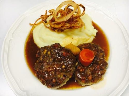 Zwei Fleischpatties mit Soße, Kartoffelpüree und karamellisierten Zwiebeln mit Karottengarnitur auf einem weißen Teller.
