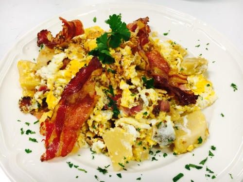Ein weißer Teller enthält ein herzhaftes Frühstück aus Rührei, knusprigem Speck und goldenen Kartoffeln, garniert mit Petersilie.