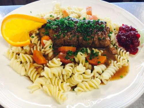 Ein Teller mit Nudeln, einem geschnittenen Steak, mit Petersilie garniert und einer Scheibe Orange, zusammen mit Cranberry-Sauce.