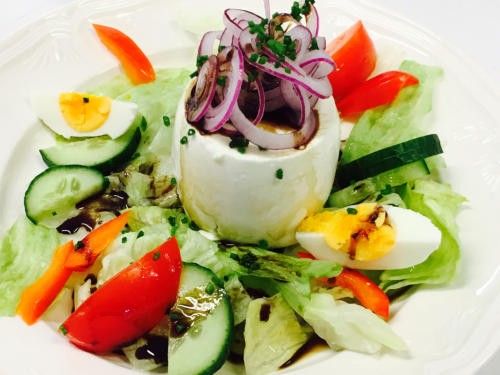 Ein Salat mit geschnittenen Gurken, Tomaten und roten Zwiebeln auf einem weißen Teller. Es gibt auch ein halbgekochtes Ei mit grünen Kräutern obenauf.