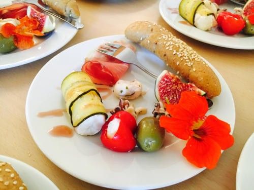Ein weißer Teller hat ein Brötchen, geschnittene Gurken, Tomaten und Oliven. Andere Teller haben Obst und Gemüse. Ein Messer und eine Gabel sind auf dem Teller.