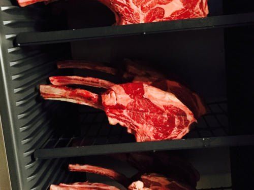 Eine Nahaufnahme mehrerer roher Rindfleischstücke, die in einem Edelstahlkühlschrank ausgestellt sind. Die Stücke variieren in Größe und Form, wobei ein Stück deutlich größer ist.