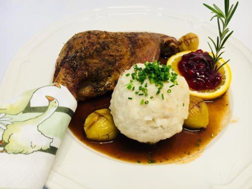Auf einem weißen Teller befindet sich ein Gericht mit gebratenem Fleisch, Kartoffelpüree und gebratenen Zwiebeln, garniert mit grünen Kräutern und Cranberry-Sauce.