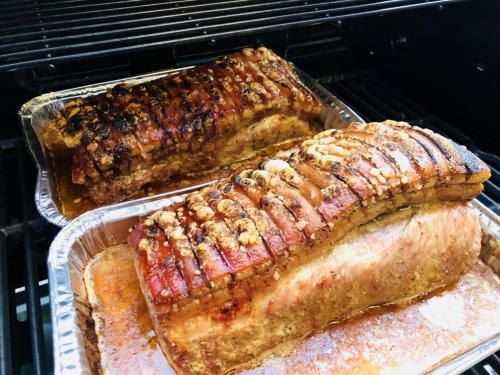 Zwei gebratene Schweinelenden in Alufolie auf einem Grill, wobei die vordere einen knusprigen, goldbraunen Krusten hat und die hintere leicht verkohlt ist.