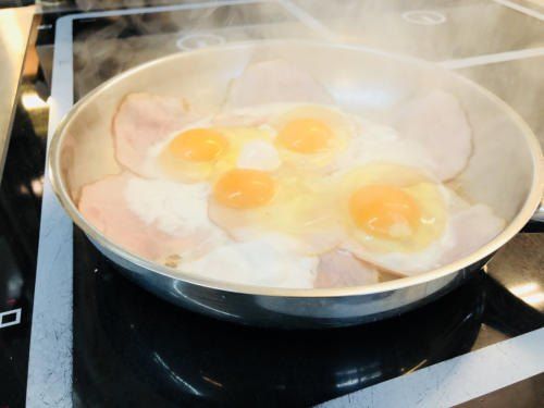 Eine Bratpfanne auf dem Herd enthält Schinken und Eier, wobei Dampf darüber aufsteigt.