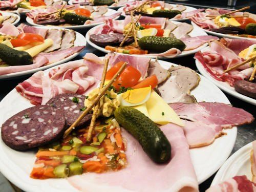 Mehrere Platten mit Charcuterie mit Fleisch, Gurken, Tomaten und Käse. Verschiedene Wurstwaren und Gemüse sind auf weißen Tellern arrangiert.