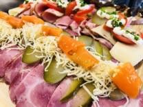 Eine Platte mit verschiedenen Fleischsorten, einschließlich Schinken, überzogen mit geriebenem Käse, Gurken und Karotten, garniert mit Tomaten und Kräutern.