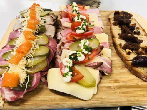 Ein Holzbrett zeigt drei Sandwiches: eines mit Fleisch, Käse, Gurken und Tomaten; ein weiteres mit Fleisch, Käse und Oliven; und ein drittes mit Fleisch, Käse und Feigen.