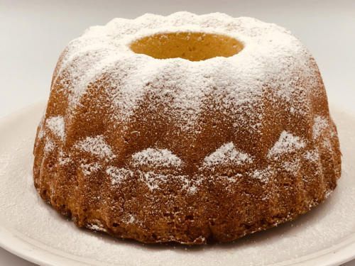 Ein Bundt-Kuchen mit Puderzucker bestreut steht auf einem weißen Teller. Er hat eine Öffnung in der Mitte.
