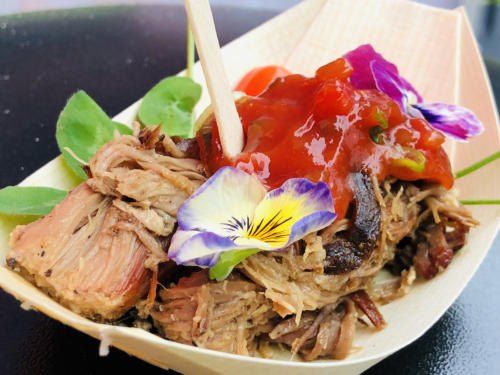Ein Gericht aus geshreddertetem Fleisch mit roter Sauce und mit Blumen garniert, serviert auf einem Papierteller mit Chopsticks.