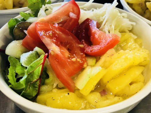 Ein weißer Bowl mit einem bunten Salat, bestehend aus frischen Tomaten, grünem Salat und Ananasstücken.