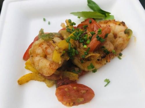 Ein weißer Teller mit Garnelen und Gemüse, garniert mit grünen Kräutern, mit einer Beilage aus geschnittenen Tomaten.