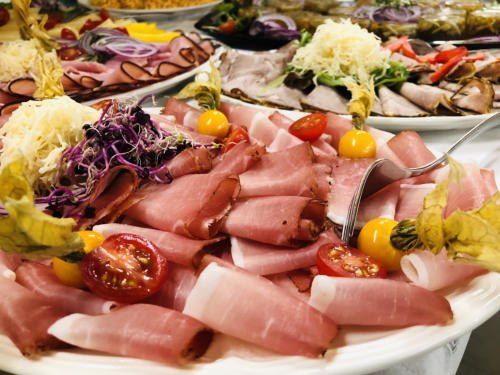 Ein Teller mit Aufschnitt, Tomaten und Garnierungen. Mehrere Platten mit verschiedenen Fleischsorten und Gemüse.