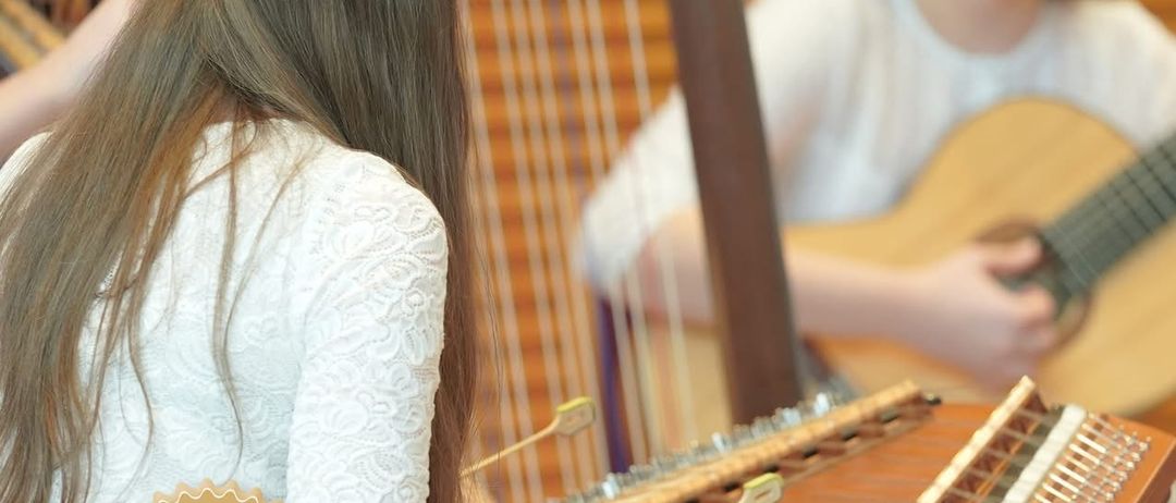 Plakat für Musikschul-Einschreibungen. Zwei Mädchen spielen Musikinstrumente, eines auf einer Harfe und das andere auf einer Gitarre. Die Daten 2025 und 2026 sind angezeigt.