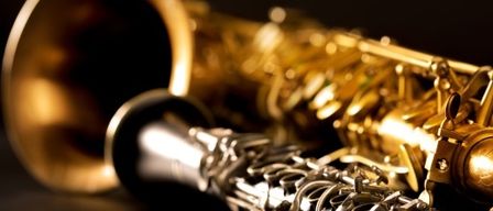 Eine Nahaufnahme eines goldenen Saxophons und einer Klarinette mit komplizierten Designs auf schwarzem Hintergrund.