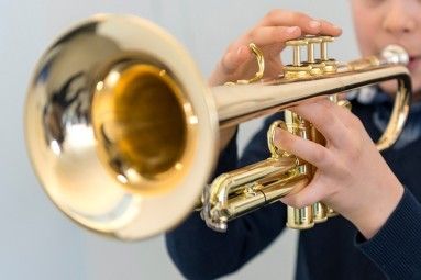 Ein junger Junge hält eine Trompete, spielt sie mit seinen Händen und trägt ein blaues Langarmshirt.