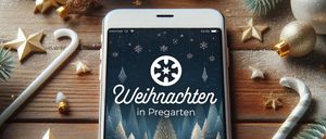 Ein weißes iPhone zeigt eine Weihnachtsszene mit einem Schneeflockenlogo und dem Text 'Weihnachten in Praegerten'. Der Bildschirm zeigt Schneemänner und eine verschneite Landschaft. Das Telefon liegt auf einer Holzoberfläche mit Weihnachtsdekoration.