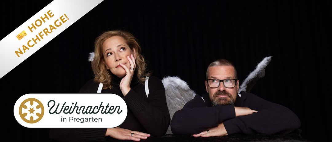 Ein Mann und eine Frau sitzen nebeneinander in schwarzer Kleidung und mit Brille. Sie posieren für ein Foto mit schwarzem Hintergrund und die Frau hat Engelsflügel.