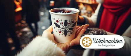 Eine Hand hält einen Becher mit festlichem Design, gefüllt mit heißem Gewürzgetränk, vor einem unscharfen Hintergrund.