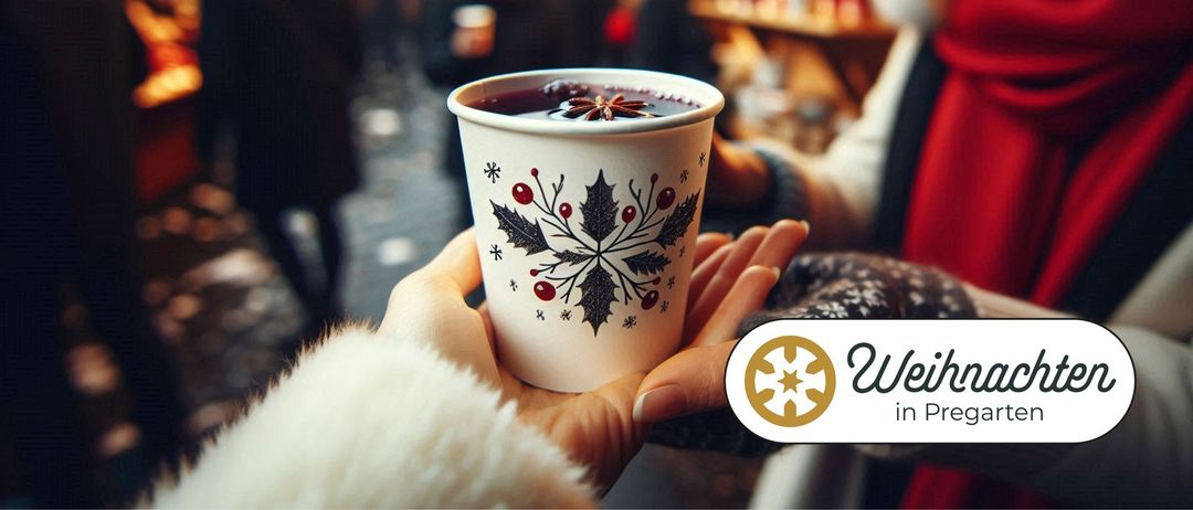 Eine Hand hält einen Becher mit festlichem Design, gefüllt mit heißem Gewürzgetränk, vor einem unscharfen Hintergrund.