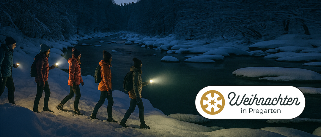 Zwei Personen gehen bei Nacht in der Nähe eines Flusses, tragen Winterkleidung und Rucksäcke. Einer hält eine Taschenlampe und beleuchtet den Weg. Schnee bedeckt den Boden und die Felsen.