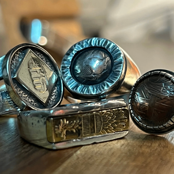 Eine Sammlung von Vintage-Ringen aus Silber und Gold mit komplizierten Designs, einschließlich eines Diamanten, eines menschlichen Gesichts und eines Kreuzes. Die Ringe sind auf einer Holzoberfläche ausgestellt.