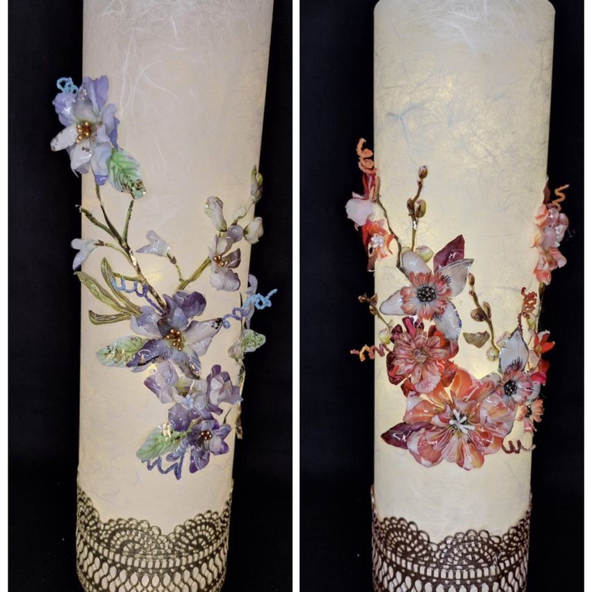 Two cylindrical objects decorated with floral designs. One has purple flowers and leaves, the other has pink and orange flowers. Both have lace-like patterns at the bottom.