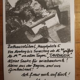 Ein Schwarz-Weiß-Bild zeigt ein Plakat mit einer Bank, Felsen und Pflanzen. Das Plakat hat Text auf Deutsch. Es scheint eine Ankündigung für eine Veranstaltung im Rathausstube zu sein.