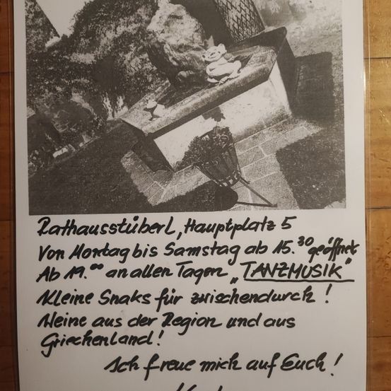 Ein Schwarz-Weiß-Bild zeigt ein Plakat mit einer Bank, Felsen und Pflanzen. Das Plakat hat Text auf Deutsch. Es scheint eine Ankündigung für eine Veranstaltung im Rathausstube zu sein.
