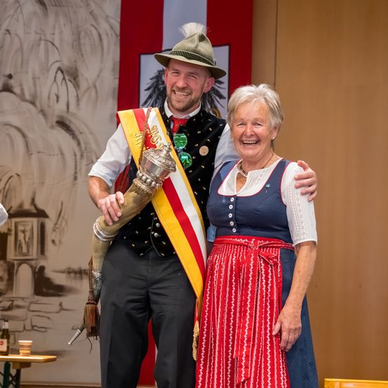 Ein Mann und eine Frau in traditioneller bayerischer Kleidung lächeln für ein Foto auf der Bühne.