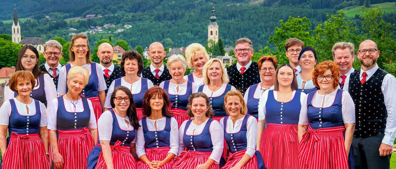 Eine Gruppe von Erwachsenen, sowohl Männer als auch Frauen, gekleidet in traditioneller Kleidung, lächeln und posieren für ein Foto vor einem bergigen Hintergrund.