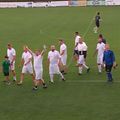Eine Gruppe von Männern in weißen Trikots läuft auf einem Fußballfeld. Ein Mann hebt die Hände und ein anderer hält einen Ball. Mehrere Spieler gehen zur Mittellinie.