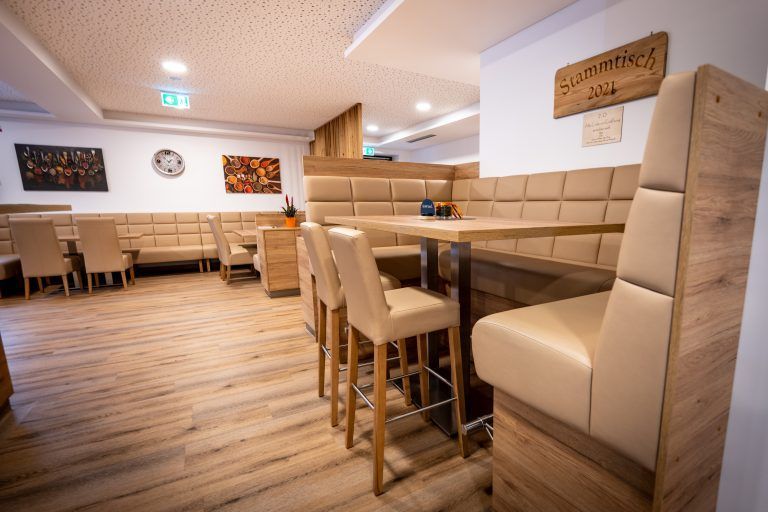 Ein Restaurant mit Holzböden, beige gepolsterten Sitzen und einem Tisch mit einem blauen Cap. An den Wänden befinden sich Bilderrahmen und ein Holzschild.