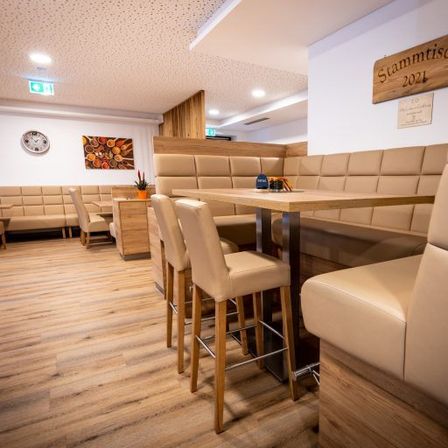 Ein Restaurant mit Holzböden, beige gepolsterten Sitzen und einem Tisch mit einem blauen Cap. An den Wänden befinden sich Bilderrahmen und ein Holzschild.