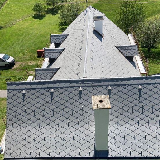 Luftaufnahme eines Hauses mit Schieferdach, Schornstein und einem weißen Lieferwagen, der auf dem Rasen geparkt ist.