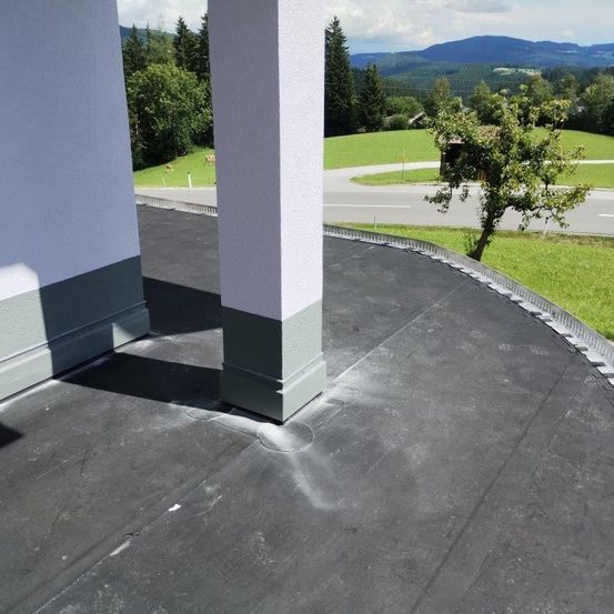 Ein Dach mit schwarzen Dachplatten, einem weißen und grauen Pfeiler und einer Straße mit einer Kurve und einem grünen Feld im Hintergrund.