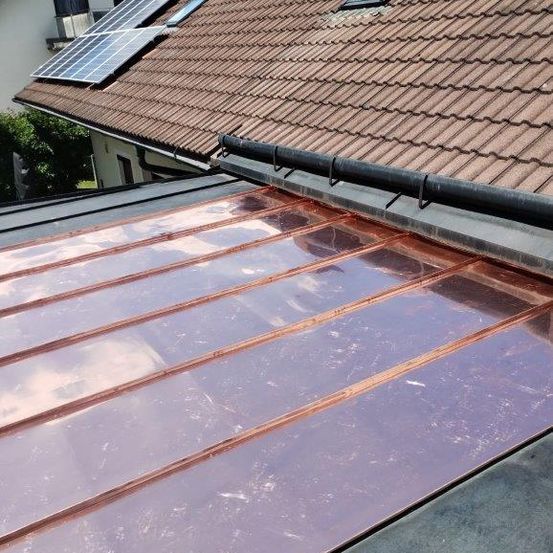 Ein Haus mit einem braunen Ziegeldach, Solarmodulen und einem kupferfarbenen Metalldach.