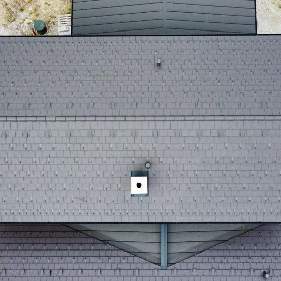 Eine Dachansicht eines modernen Hauses mit grauen Ziegeln und einem Oberlicht. Das Dach ist einheitlich ohne sichtbare Schäden.
