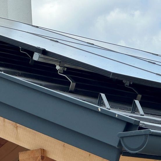 Ein Nahaufnahme einer Solarpanel-Installation auf einem Hausdach. Das Solarpanel ist mit Metallhalterungen am Dach befestigt.