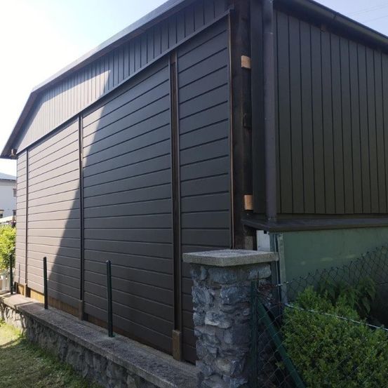 Eine schwarze Außenseite eines Hauses mit einem Metallzaun und einem Steinpfeiler an der Seite.