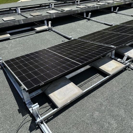Eine Draufsicht auf Solarmodule, die auf einem Metallgestell auf dem Dach montiert sind. Die Module sind schwarz und rechteckig.