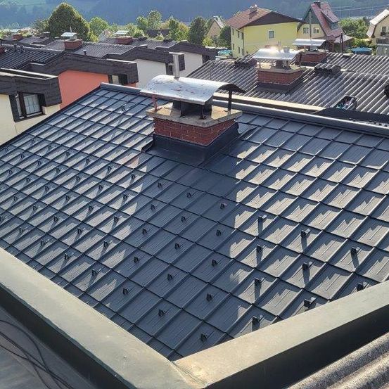 Luftaufnahme einer Nachbarschaft mit Häusern und Dächern. Einige haben Schornsteine und Solarpanels. Bäume und Berge sind in der Ferne.