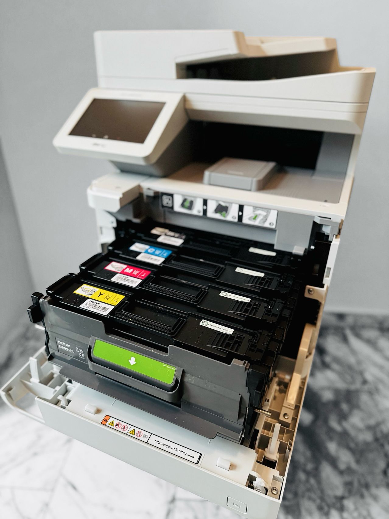 Eine Nahaufnahme eines geöffneten Multifunktionsdruckers, der seine Kartuschen zeigt. Der Drucker hat eine Glasplatte und steht auf einer Marmoroberfläche.