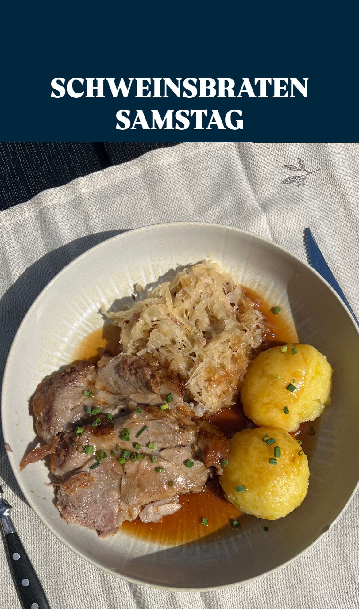 Ein Teller mit geschmorter Schweinshaxe, Sauerkraut und Kartoffelknödel, garniert mit Schnittlauch, auf einem weißen Tuch.