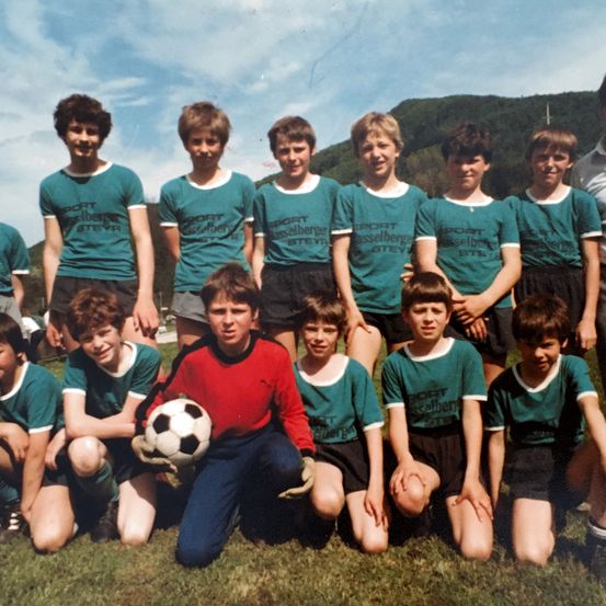 Eine Gruppe junger Jungen in grünen und roten Trikots posiert für ein Teamfoto, wobei ein Junge einen Fußball hält.
