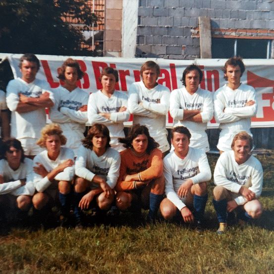 Eine Gruppe von Fußballspielern posiert für ein Mannschaftsfoto auf einem Rasenfeld mit einem Banner im Hintergrund.