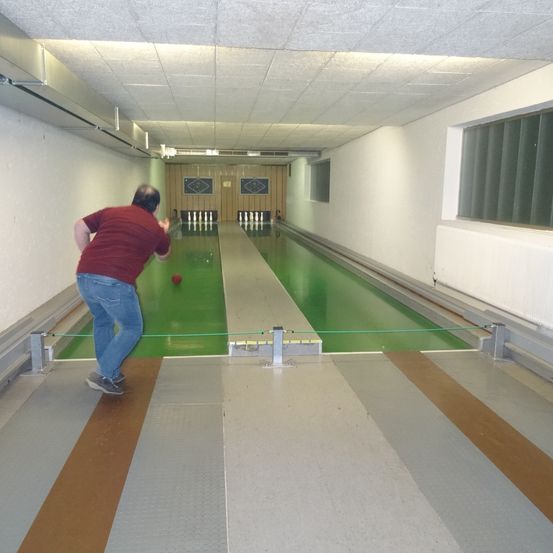 Ein Mann wirft einen Bowlingball die Bahn in einer Bowlingbahn hinunter. Die grüne Bahn hat einen weißen Rand.